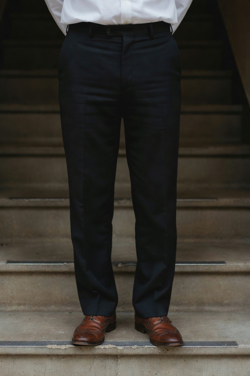 Man standing confidently on concrete stairs in a crisp white dress shirt tucked into tailored black wool trousers paired with polished brown leather dress shoes, evoking timeless professional poise