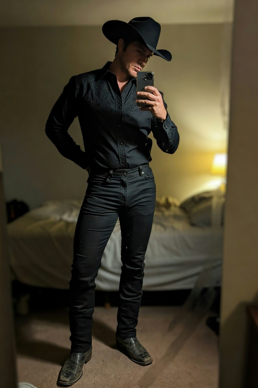 Man taking mirror selfie in all-black cowboy outfit: black cowboy hat, embroidered black button-up shirt unbuttoned at collar, slim black jeans, black cowboy boots, standing confidently in bedroom