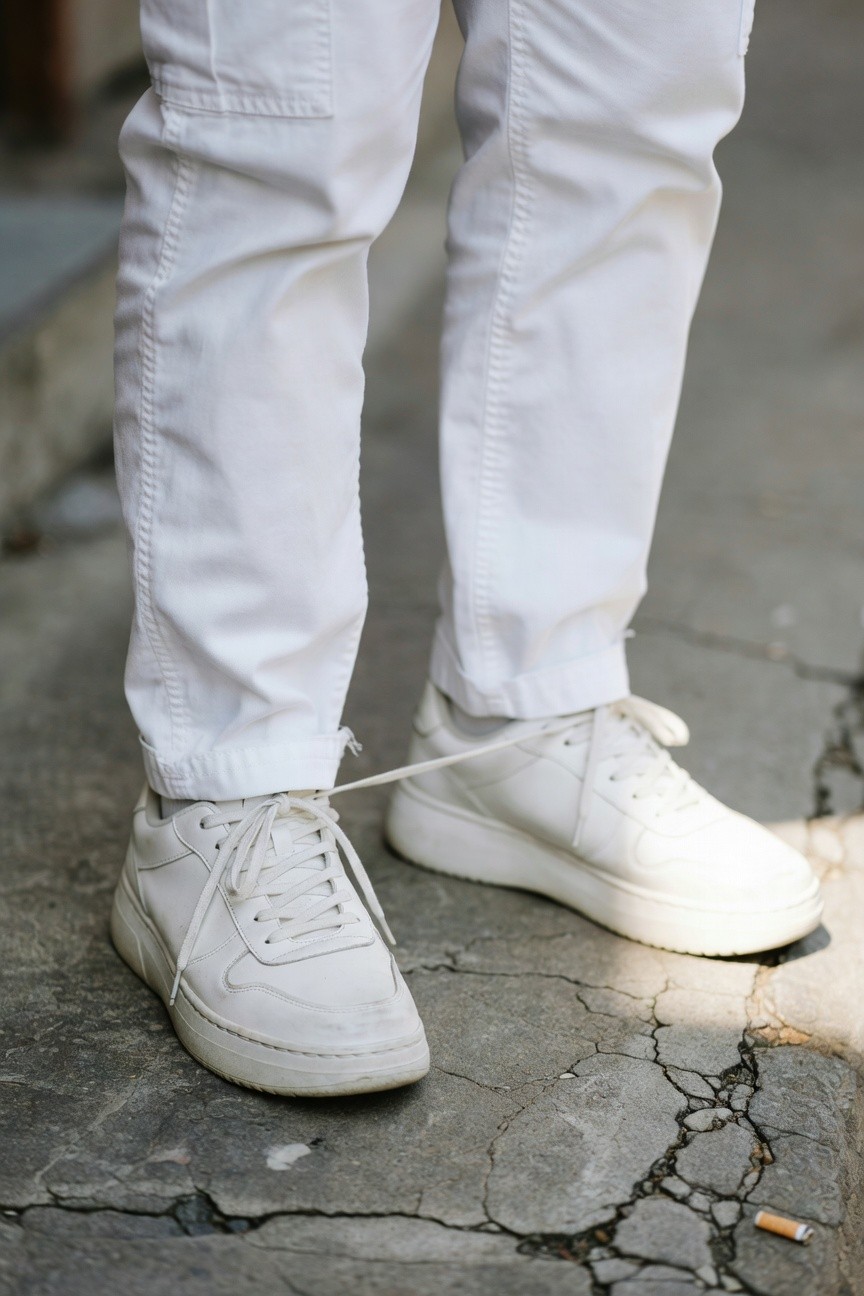 Close-up of white cargo pants with utility pockets tucked into chunky white platform sneakers on uneven stone pavement, evoking casual street style