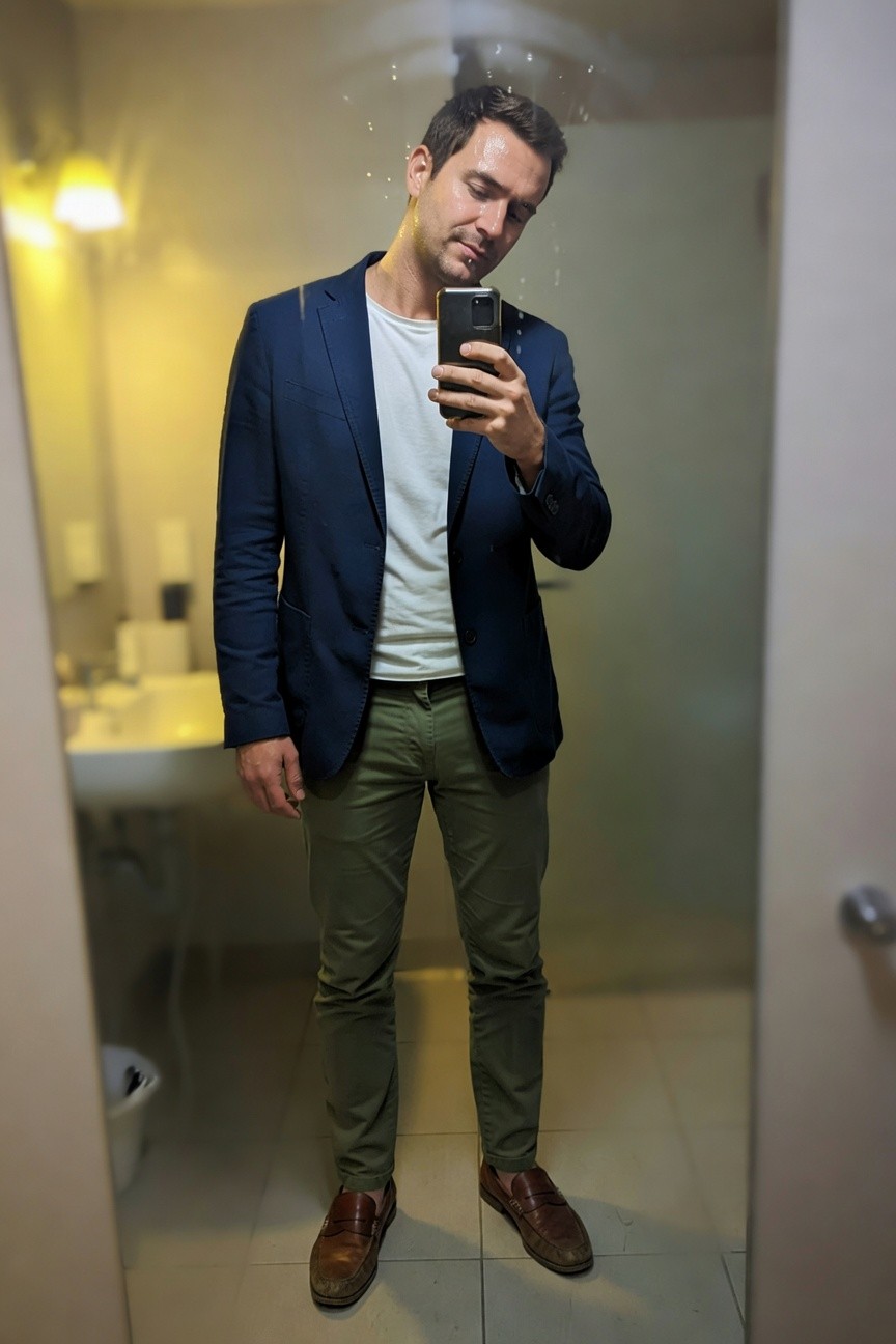 Man taking mirror selfie in bathroom wearing navy blue blazer over white t-shirt olive green chinos and brown loafers casual smart vibe