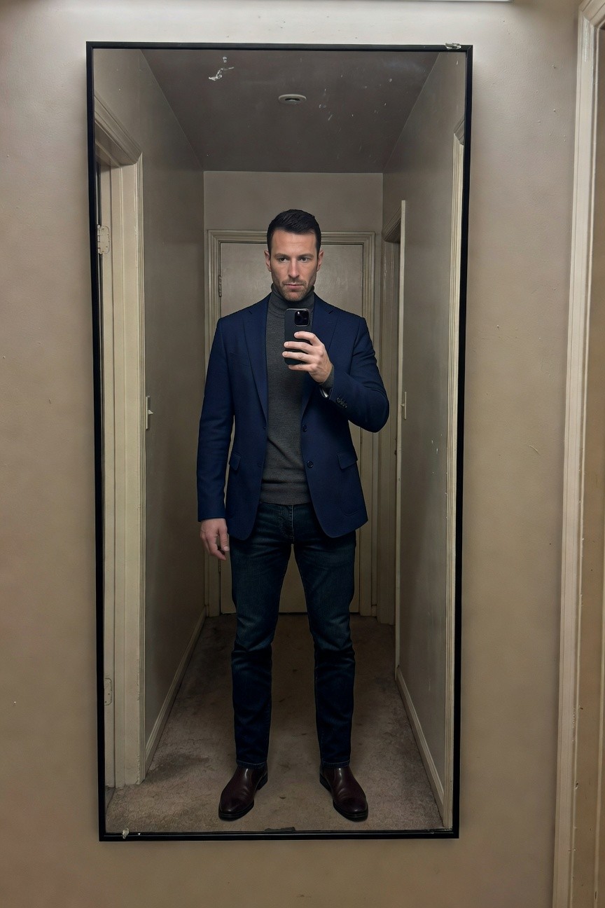 Man in navy blue blazer over gray turtleneck sweater, dark blue jeans, and brown leather boots, selfie in hallway mirror
