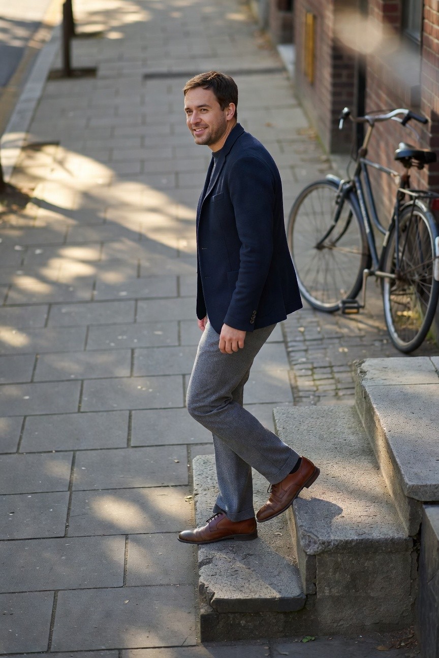 Man in slim light grey wool pants, navy blazer, and polished brown leather oxfords walking up stone steps, business casual style