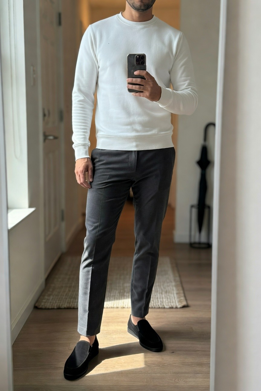 Man in white ribbed-cuff crewneck sweater, slim grey trousers, and black suede loafers, standing in a hallway mirror selfie for a minimalist outfit