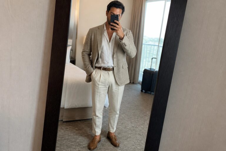 Man in beige linen suit and white shirt taking mirror selfie in hotel room