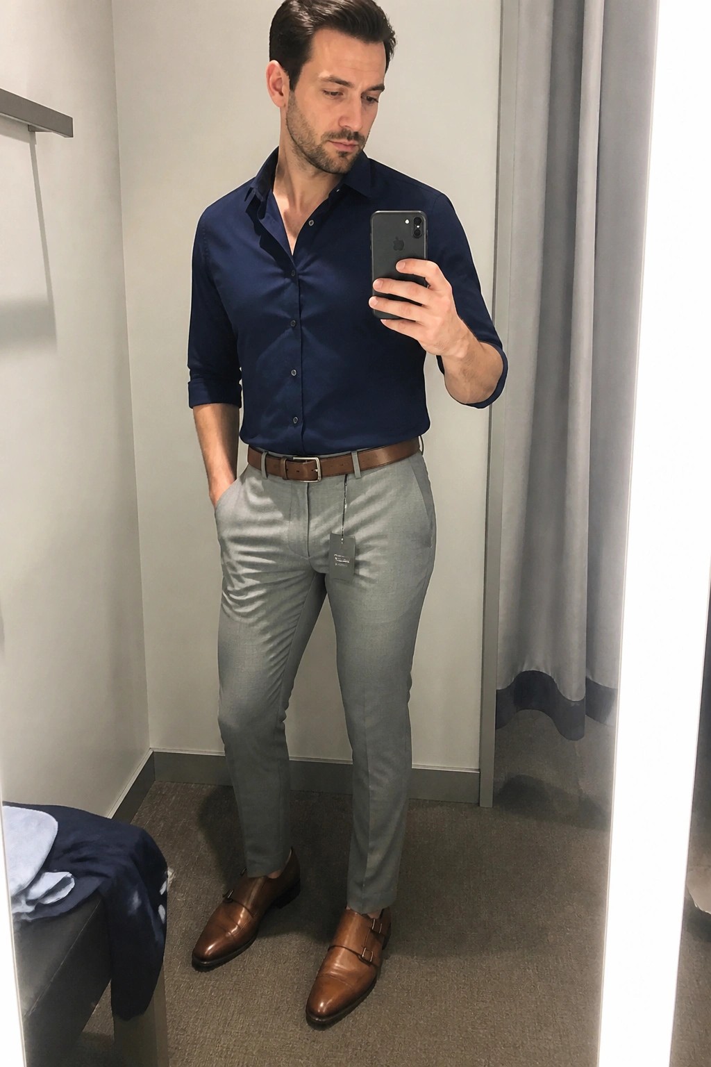 Man in navy shirt and gray pants taking mirror selfie in fitting room