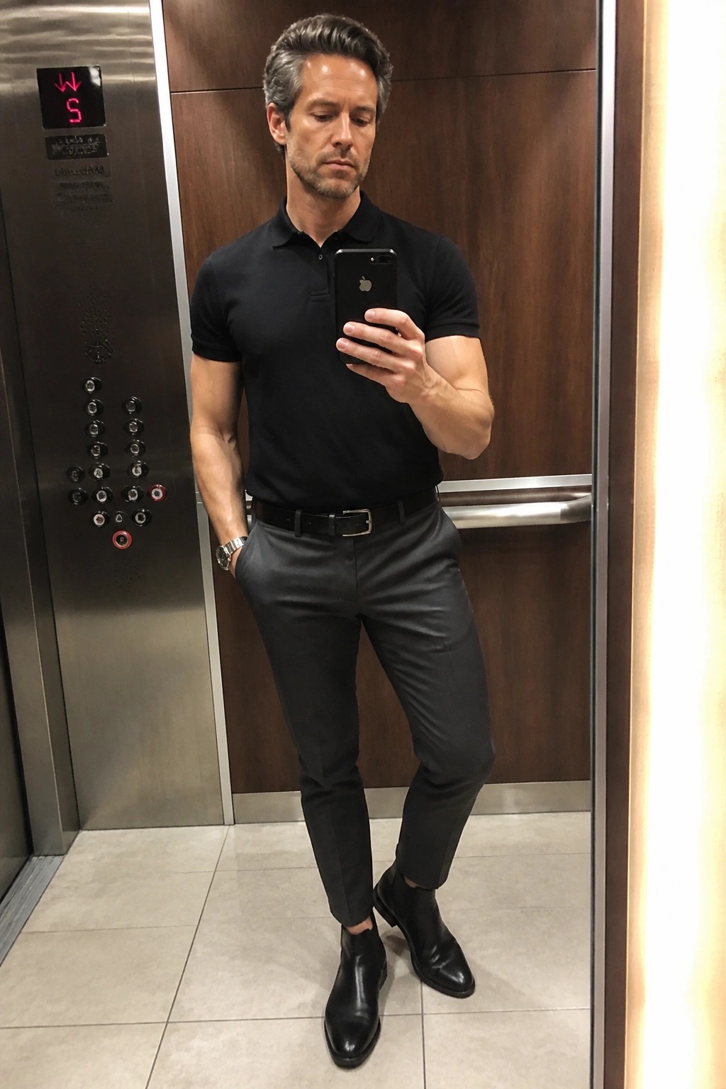 Man in black polo shirt taking mirror selfie in elevator