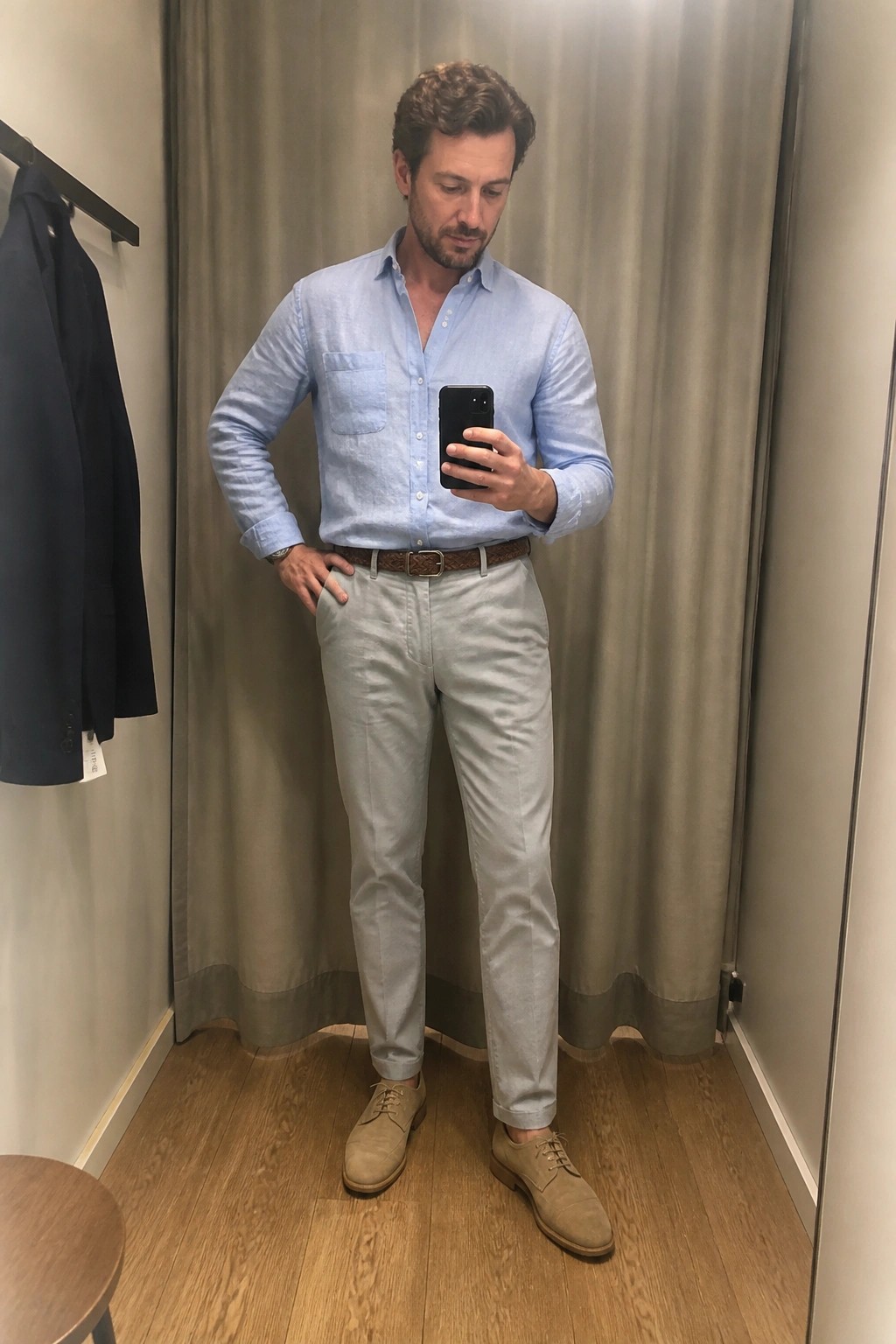 Man in light blue shirt and beige pants taking mirror selfie in fitting room