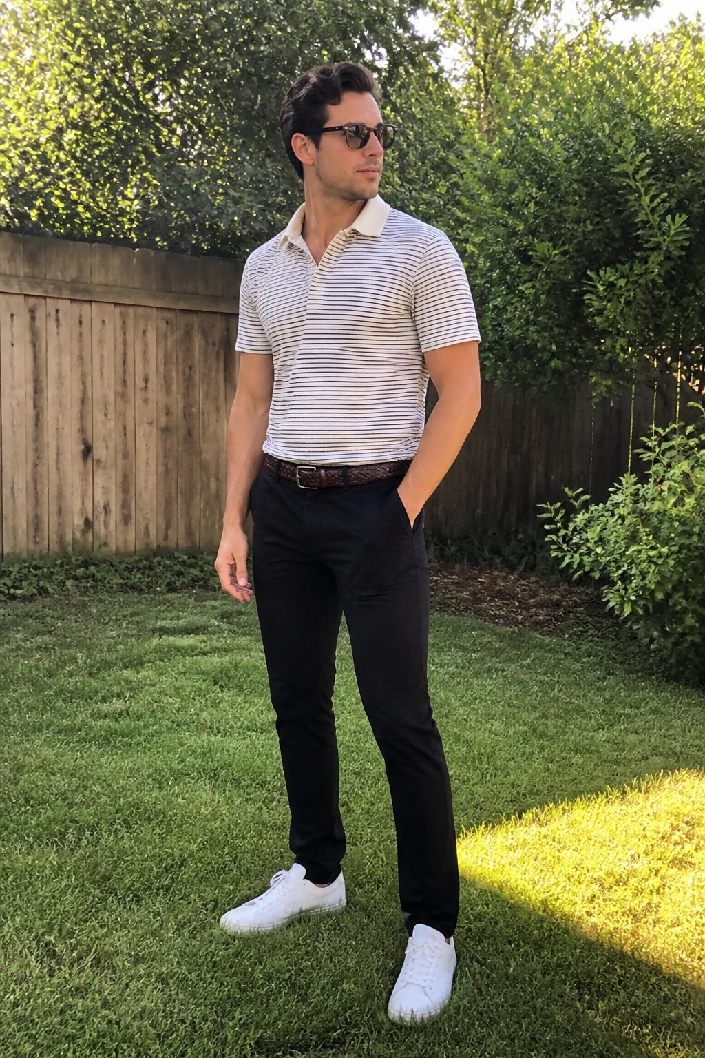 Man in striped polo shirt and black pants standing on sunny lawn