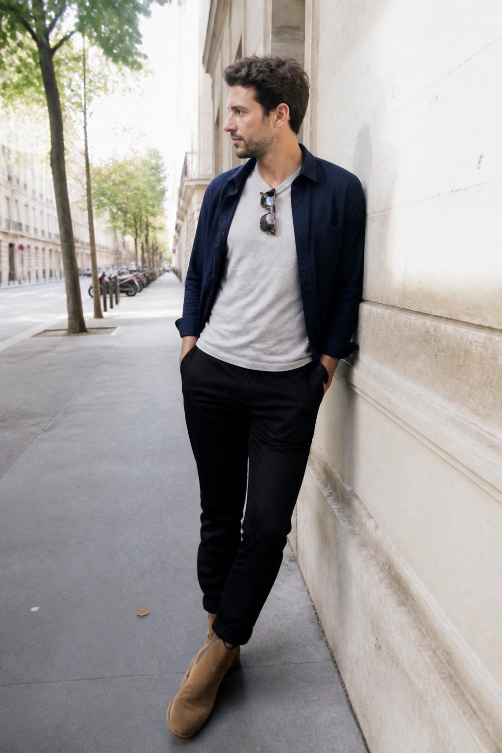 Man in navy shirt over gray tee and black pants leans on stone wall