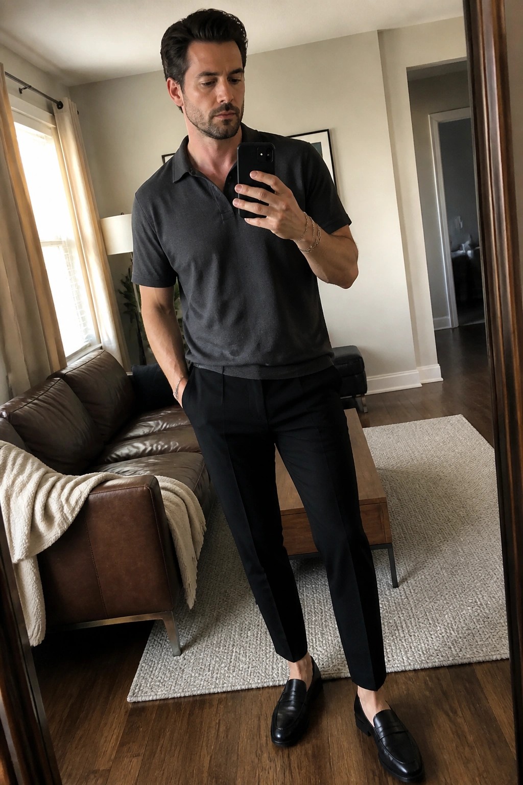 Man in gray polo shirt and black pants taking mirror selfie in living room