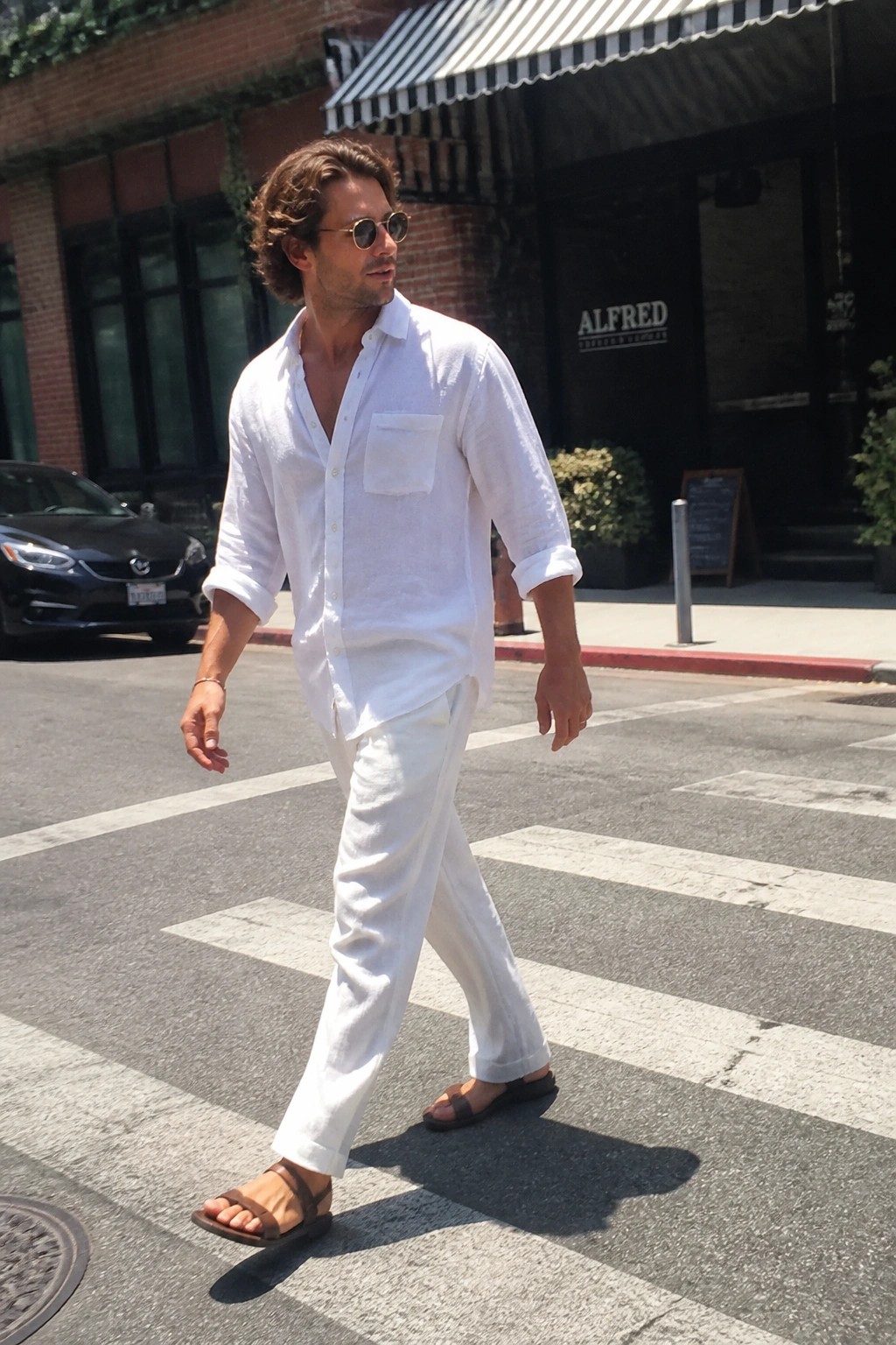 Man in white linen shirt and pants crossing sunny city crosswalk
