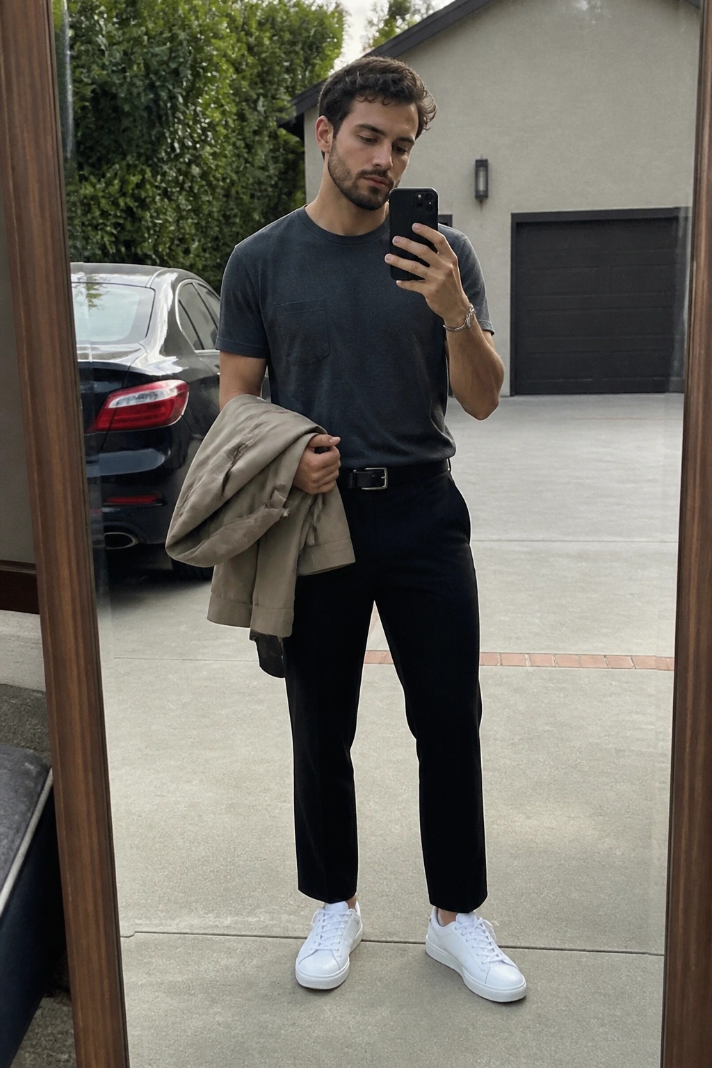 Man in gray t-shirt and black pants taking mirror selfie while holding beige jacket