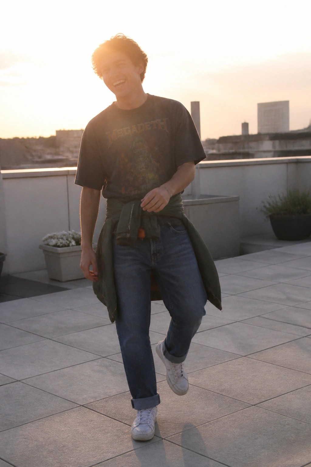 Man in Megadeth t-shirt with green jacket tied at waist on sunset rooftop