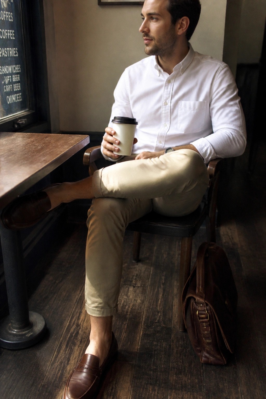 Man in white shirt and khaki pants holding coffee cup in rustic cafe