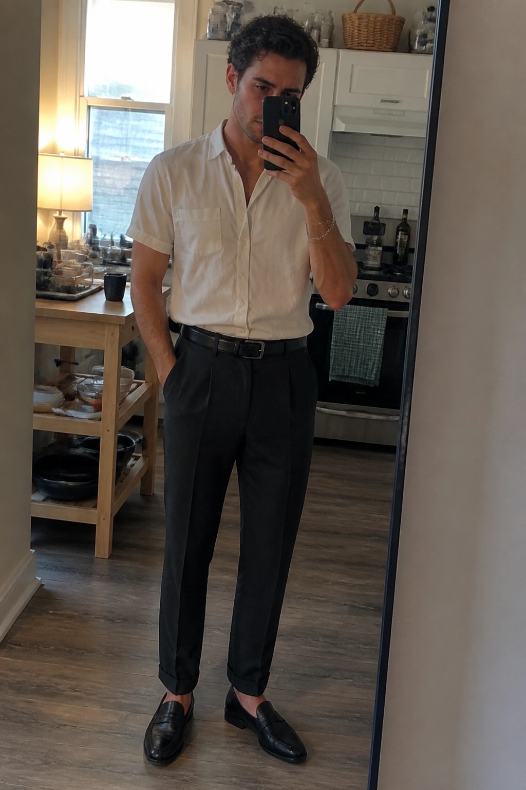 Man in white shirt and black pants taking mirror selfie in kitchen