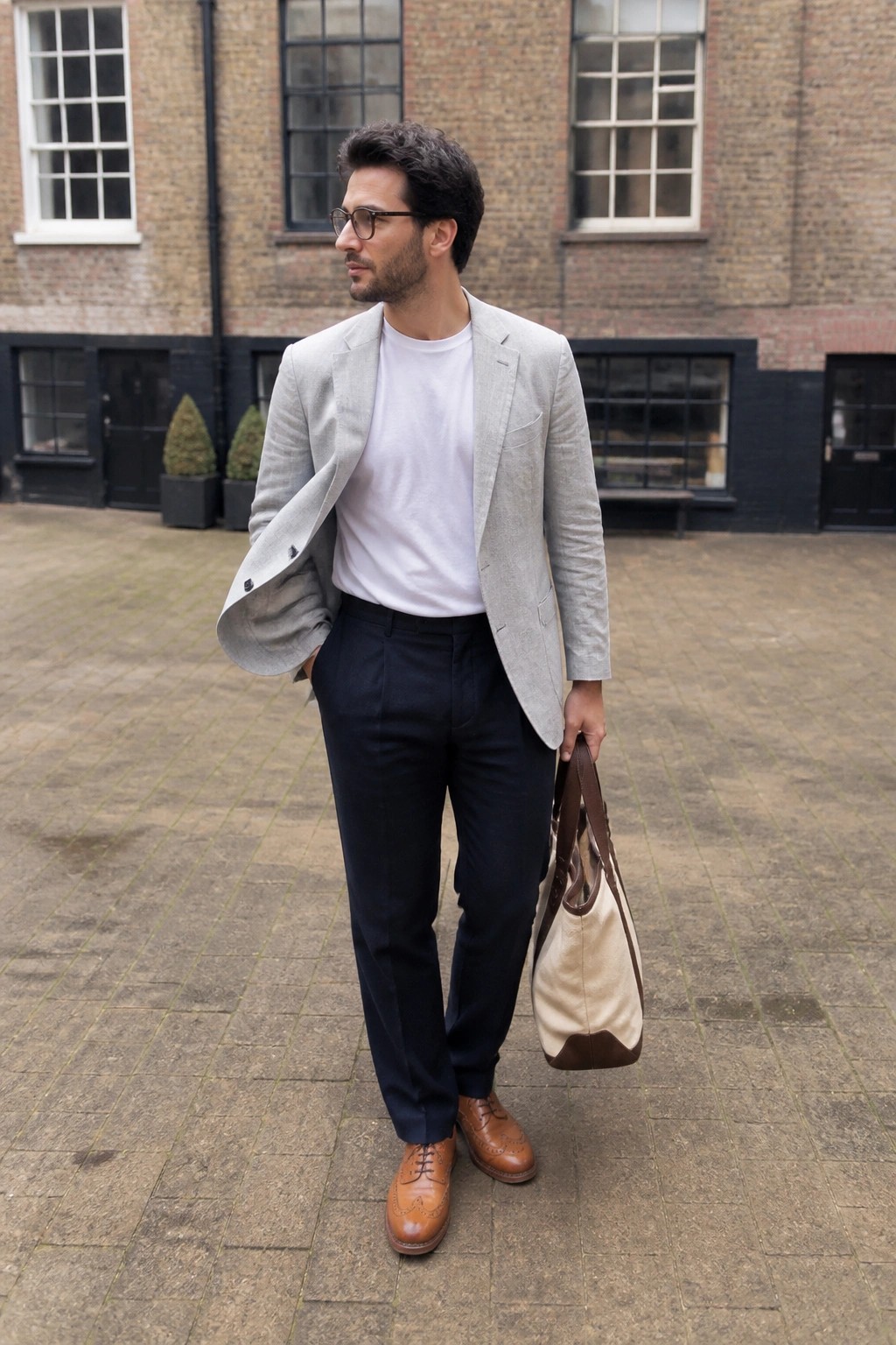 Man in light gray blazer over white t-shirt with navy pants holding tote bag outdoors