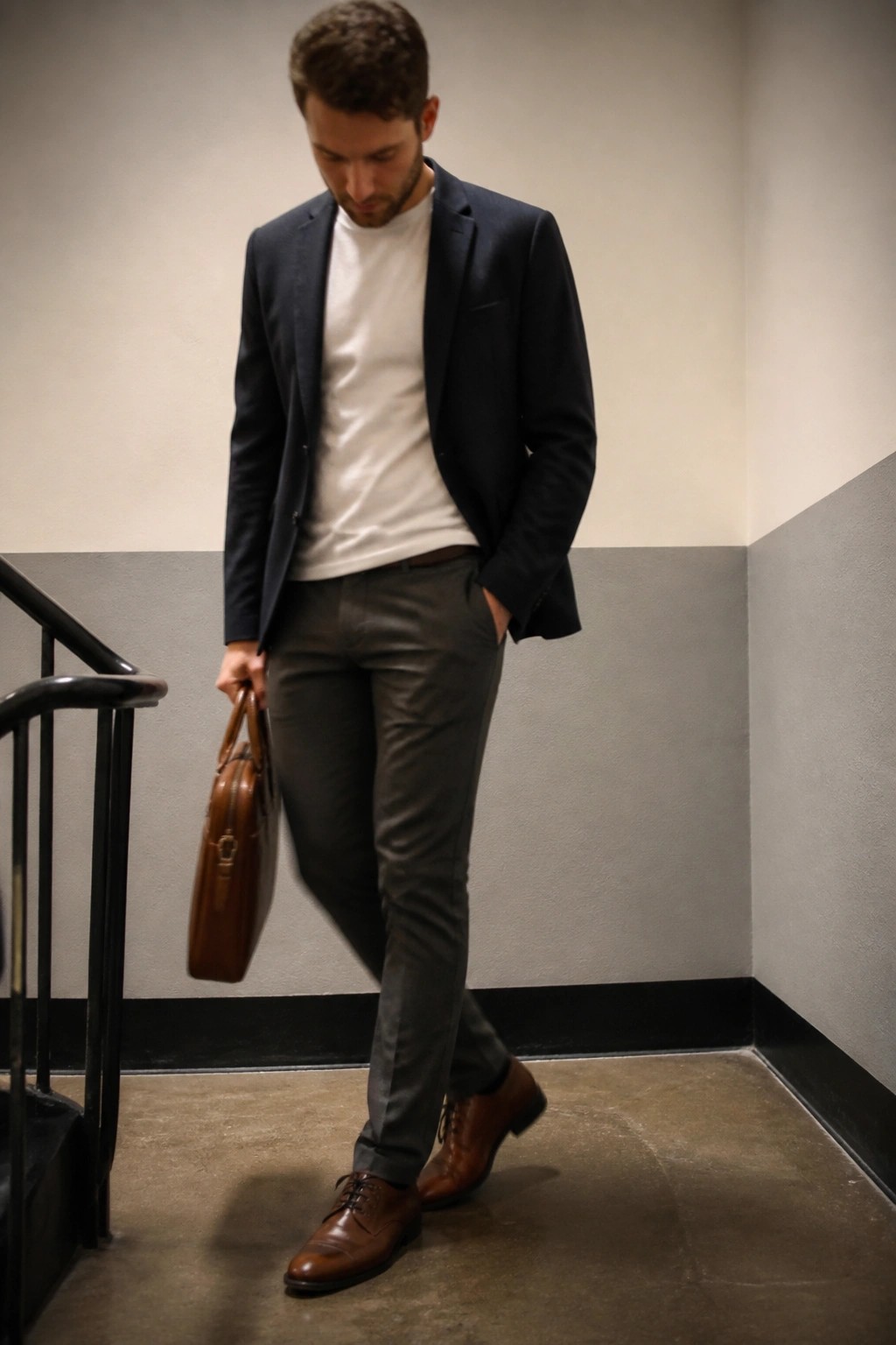 Man in navy blazer and white t-shirt carrying brown leather bag on stairs