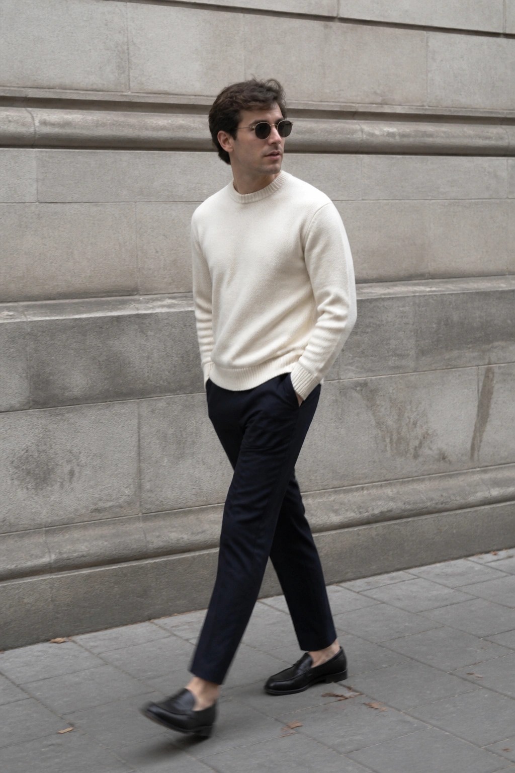 Man in cream sweater and navy pants walking by stone wall