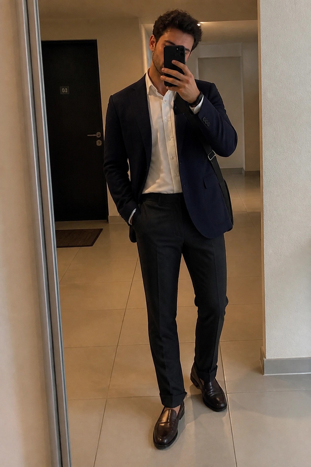 Man in navy blazer and white shirt taking mirror selfie with phone