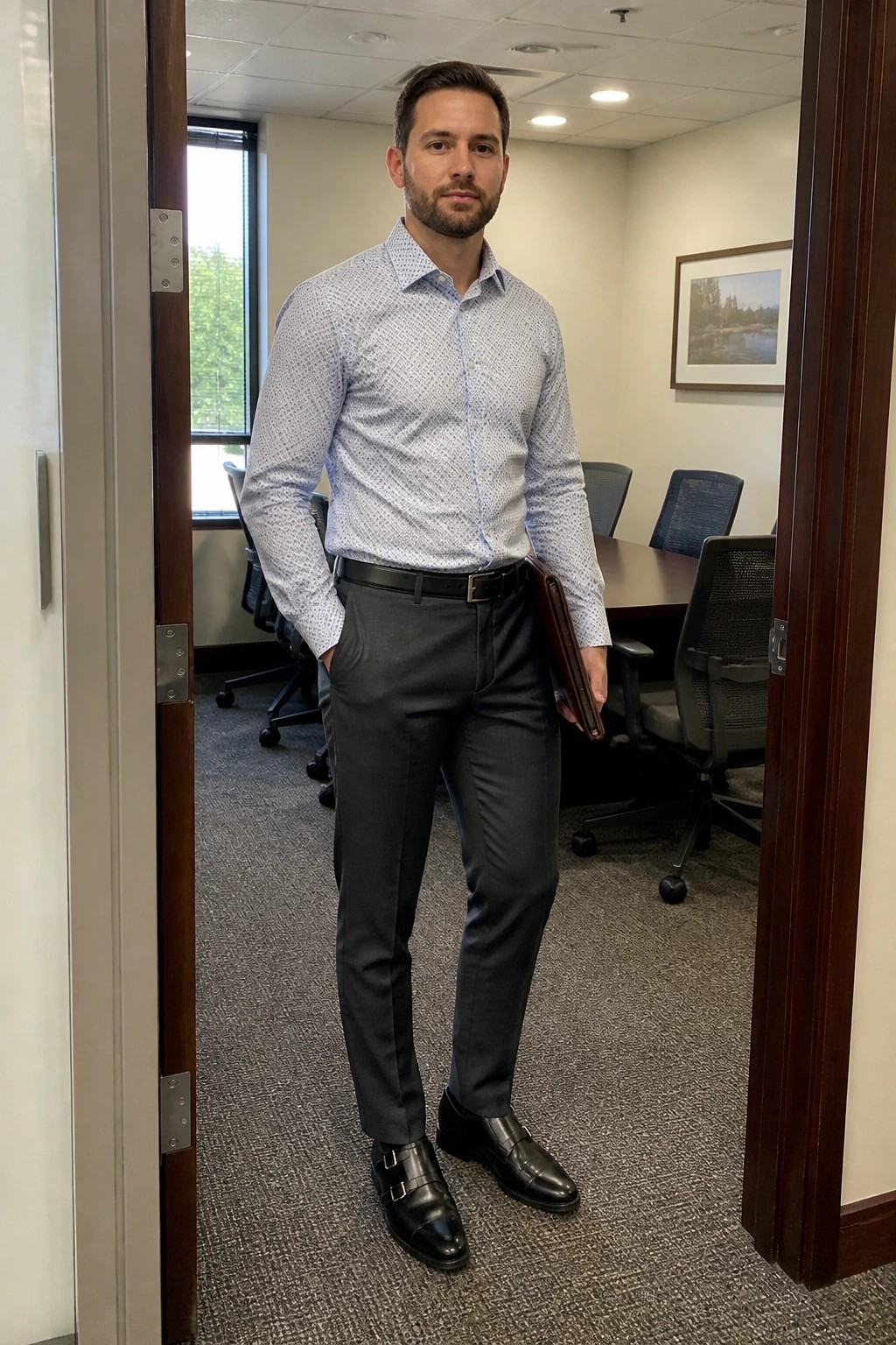 Man in blue patterned shirt and gray pants holding portfolio in office doorway