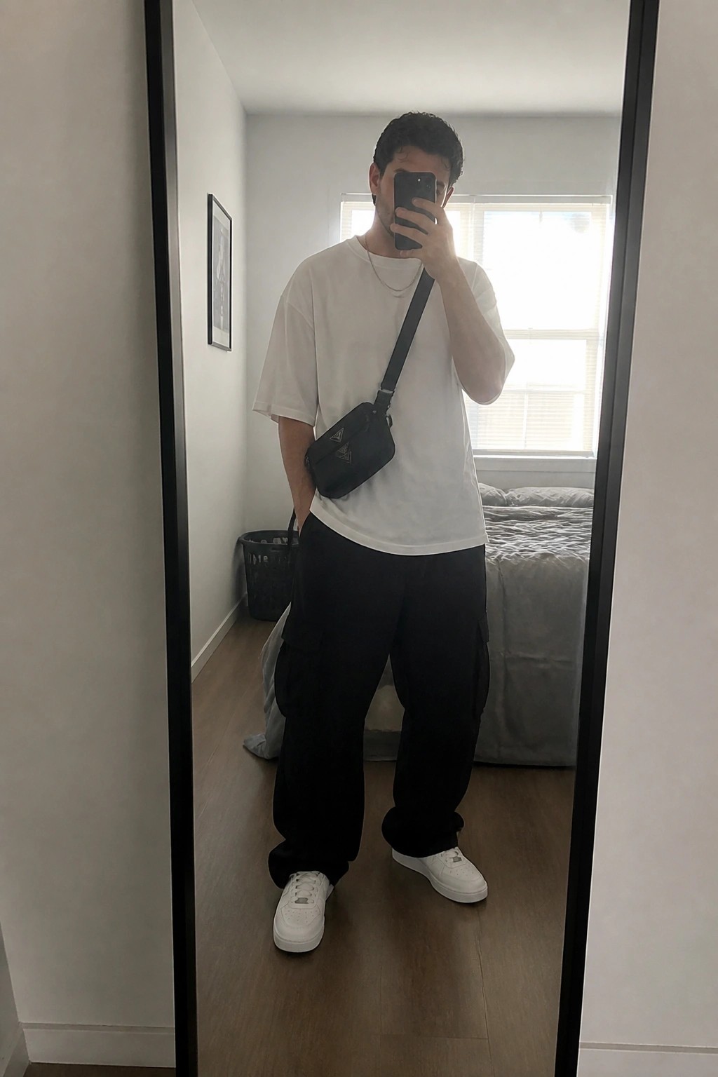 Man in white tee and black cargo pants taking mirror selfie with phone