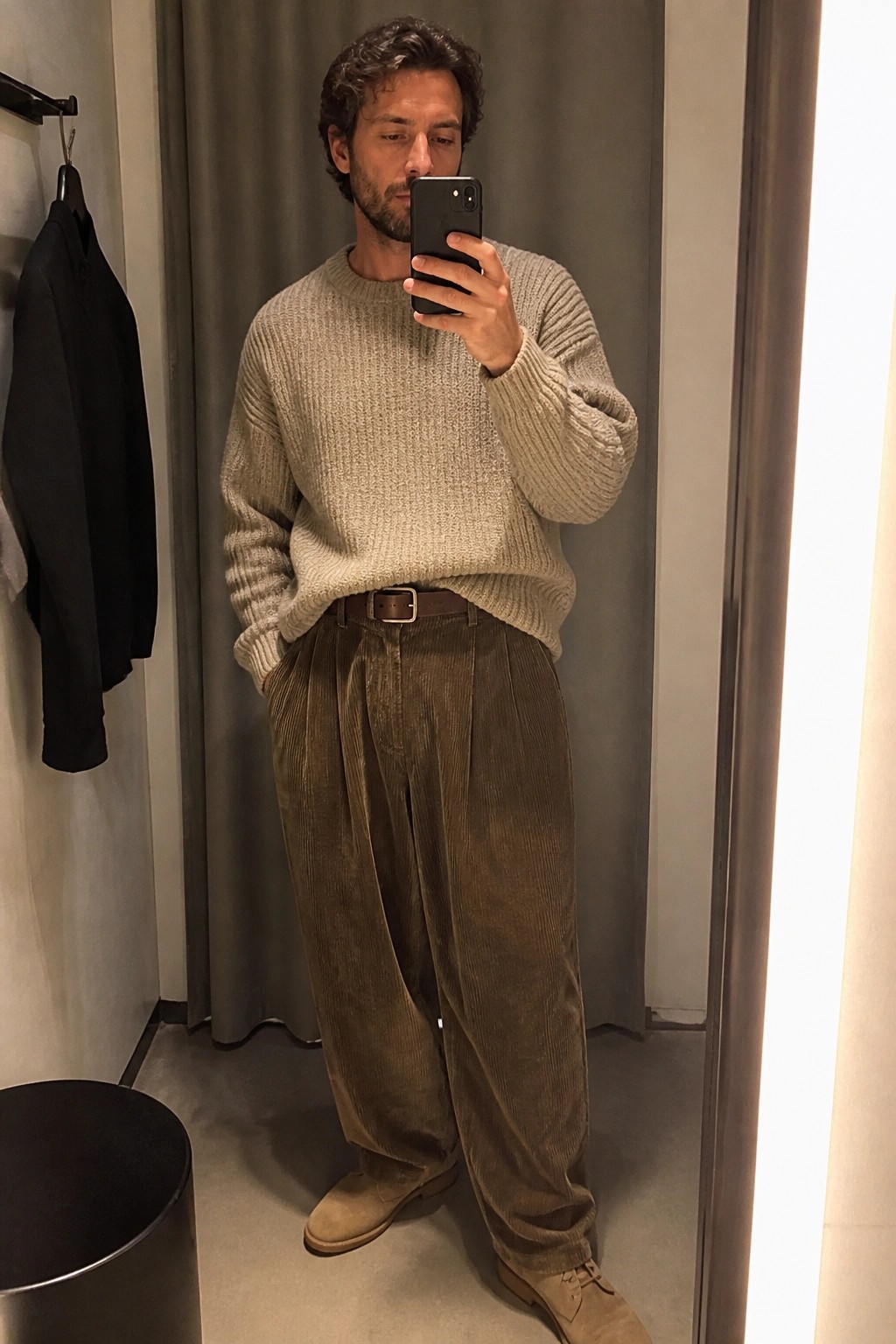 Man in mirror selfie wearing oversized beige knit sweater tucked into brown corduroy baggy pleated pants with brown belt and beige suede boots.