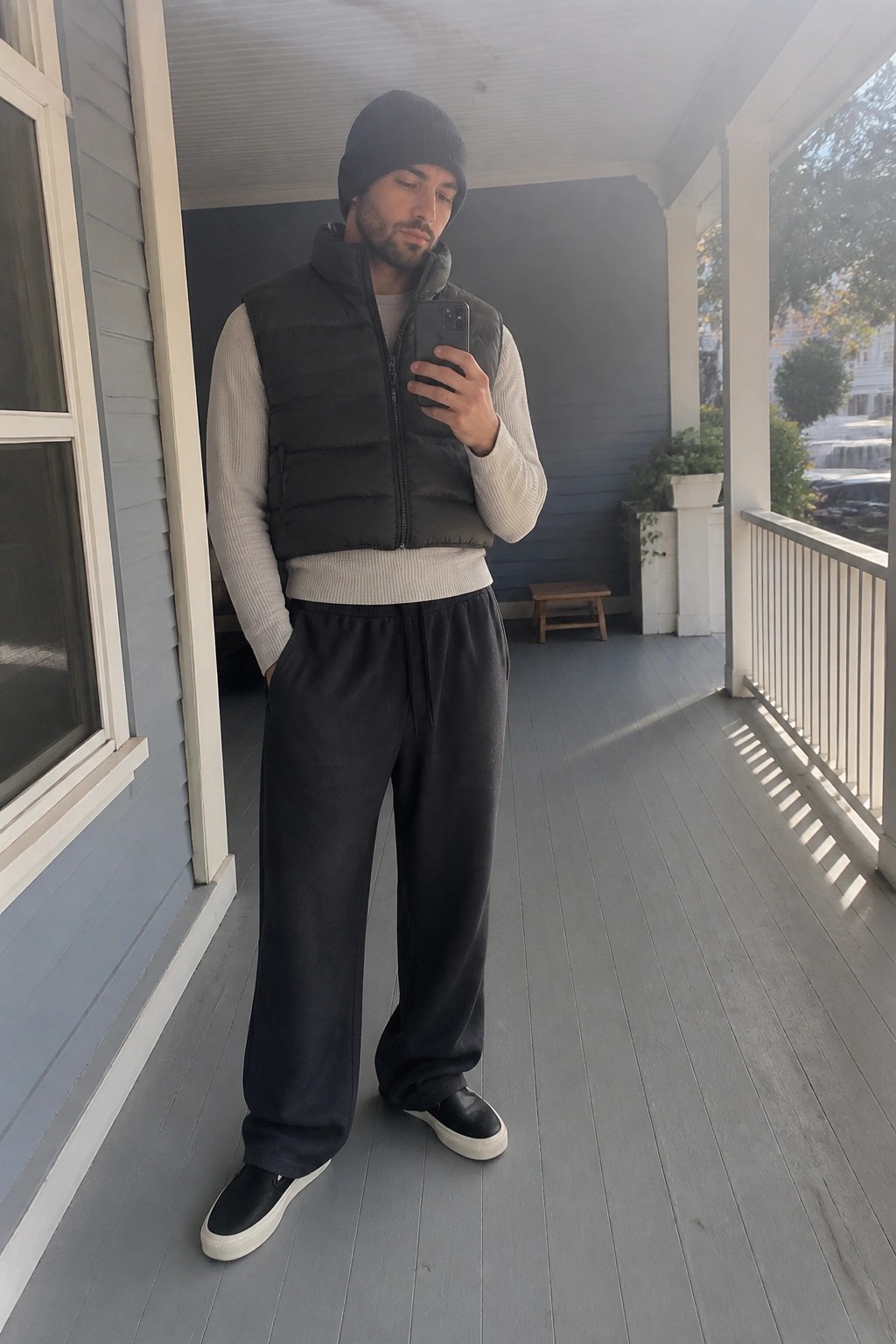 Man in black beanie and puffer vest taking selfie on porch