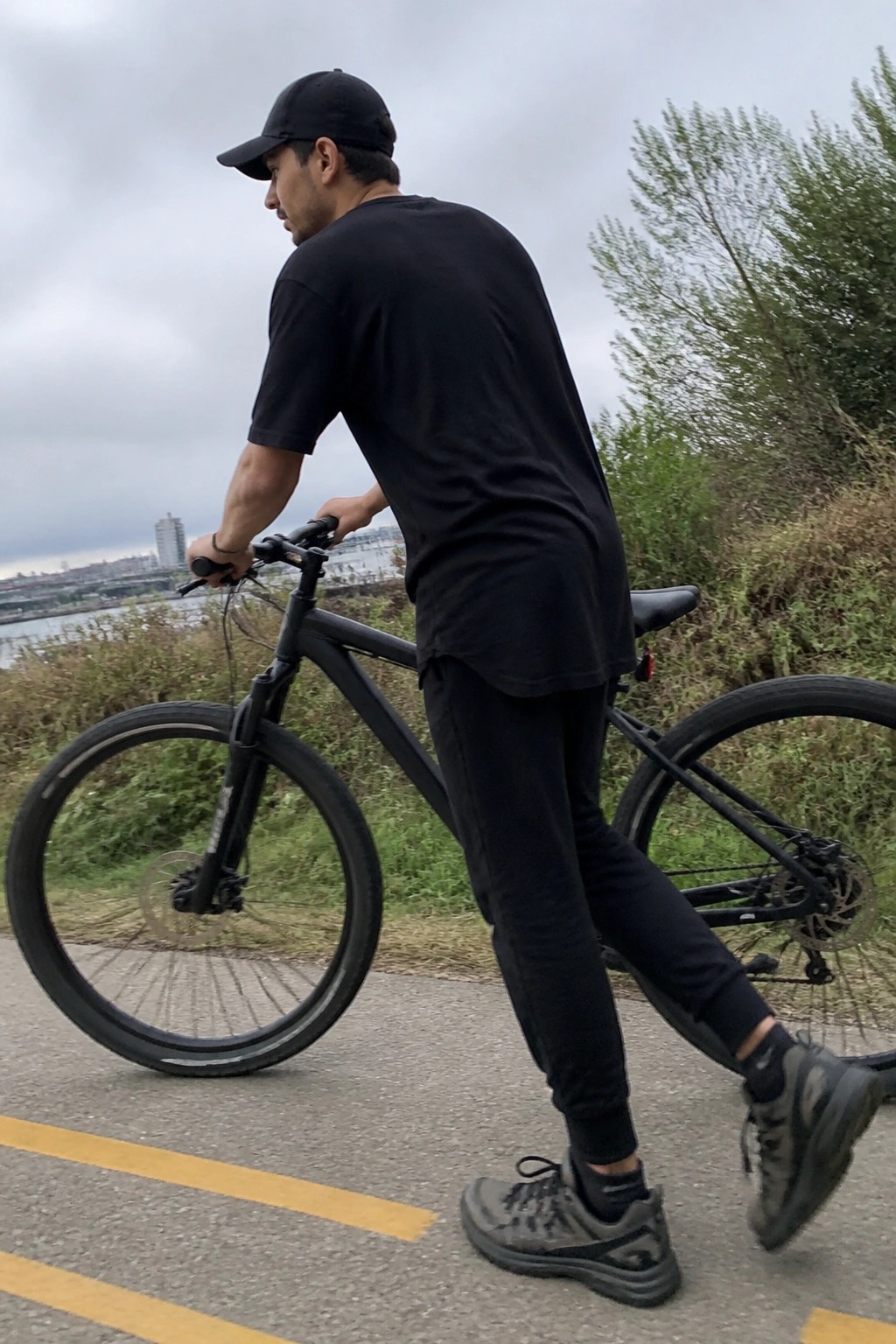 Man in black attire standing with black bicycle on yellow-lined path.