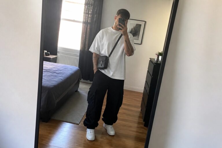 Man in white tee and black cargo pants taking mirror selfie with phone