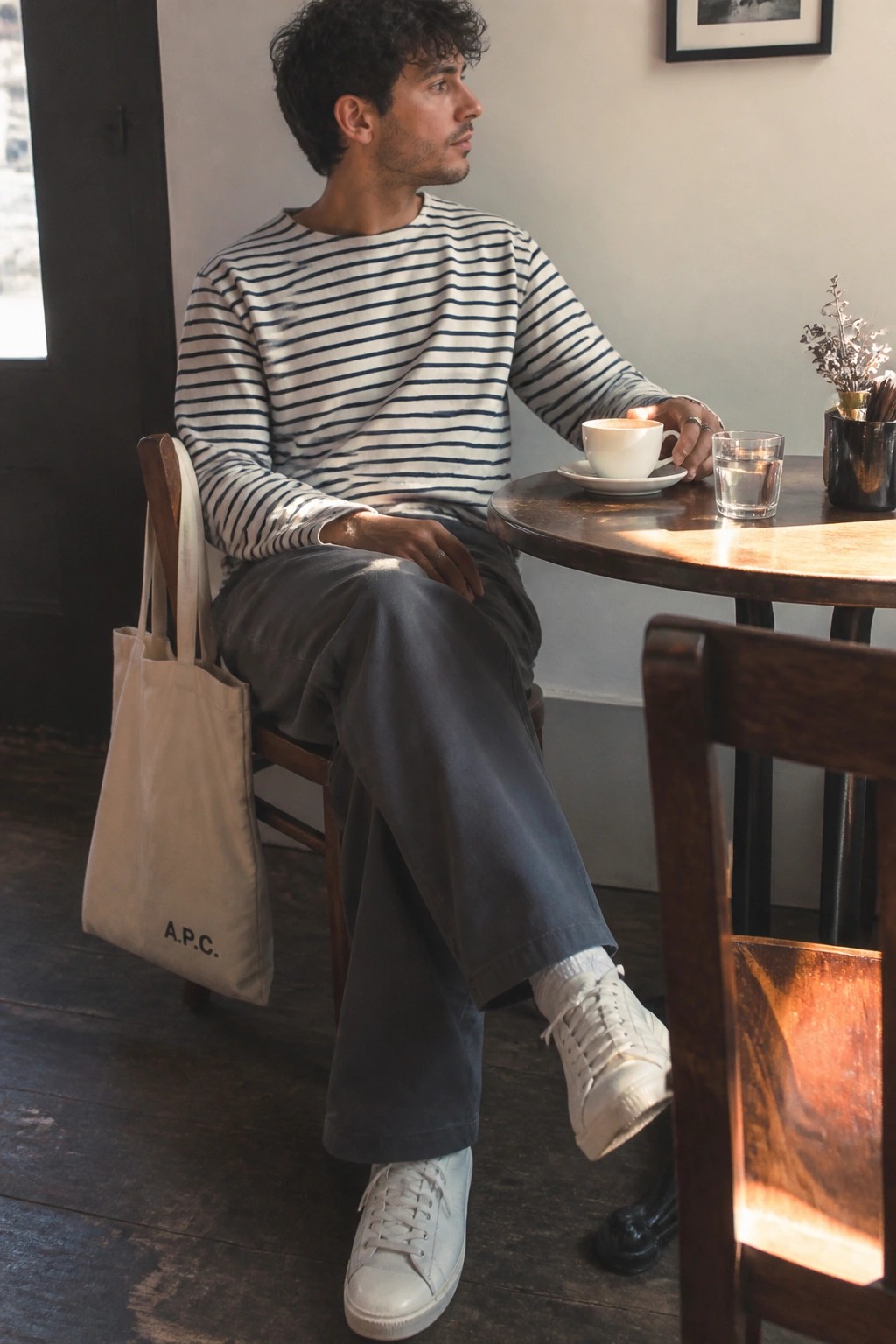 Man in striped shirt at wooden cafe table with A.P.C. tote bag and coffee