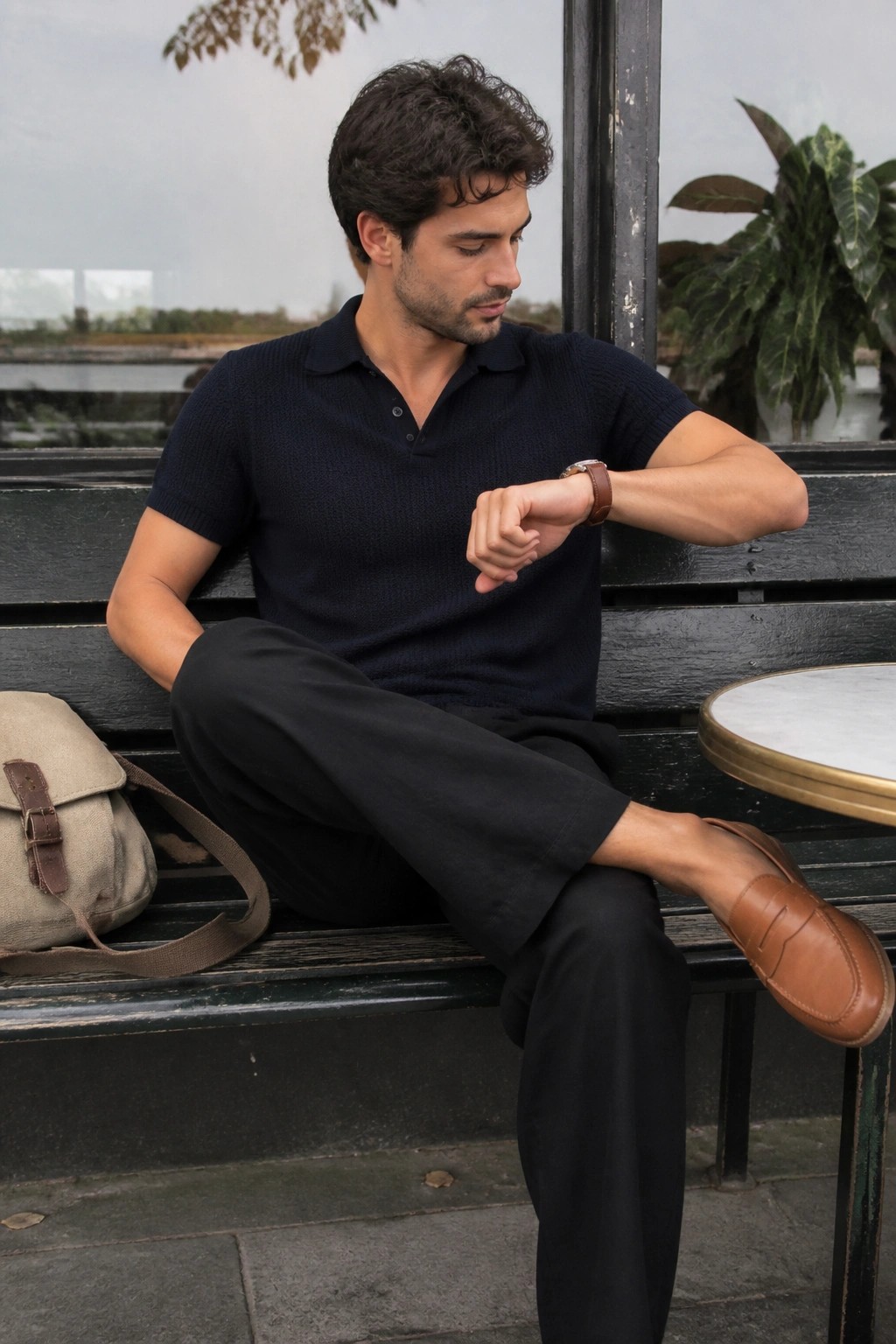 Man in navy polo shirt checks watch on outdoor bench beside beige bag.