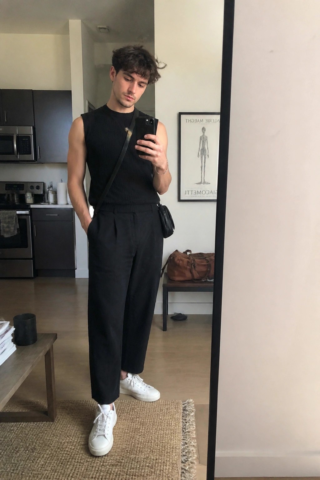 Man in black sleeveless top and wide pants taking mirror selfie with phone