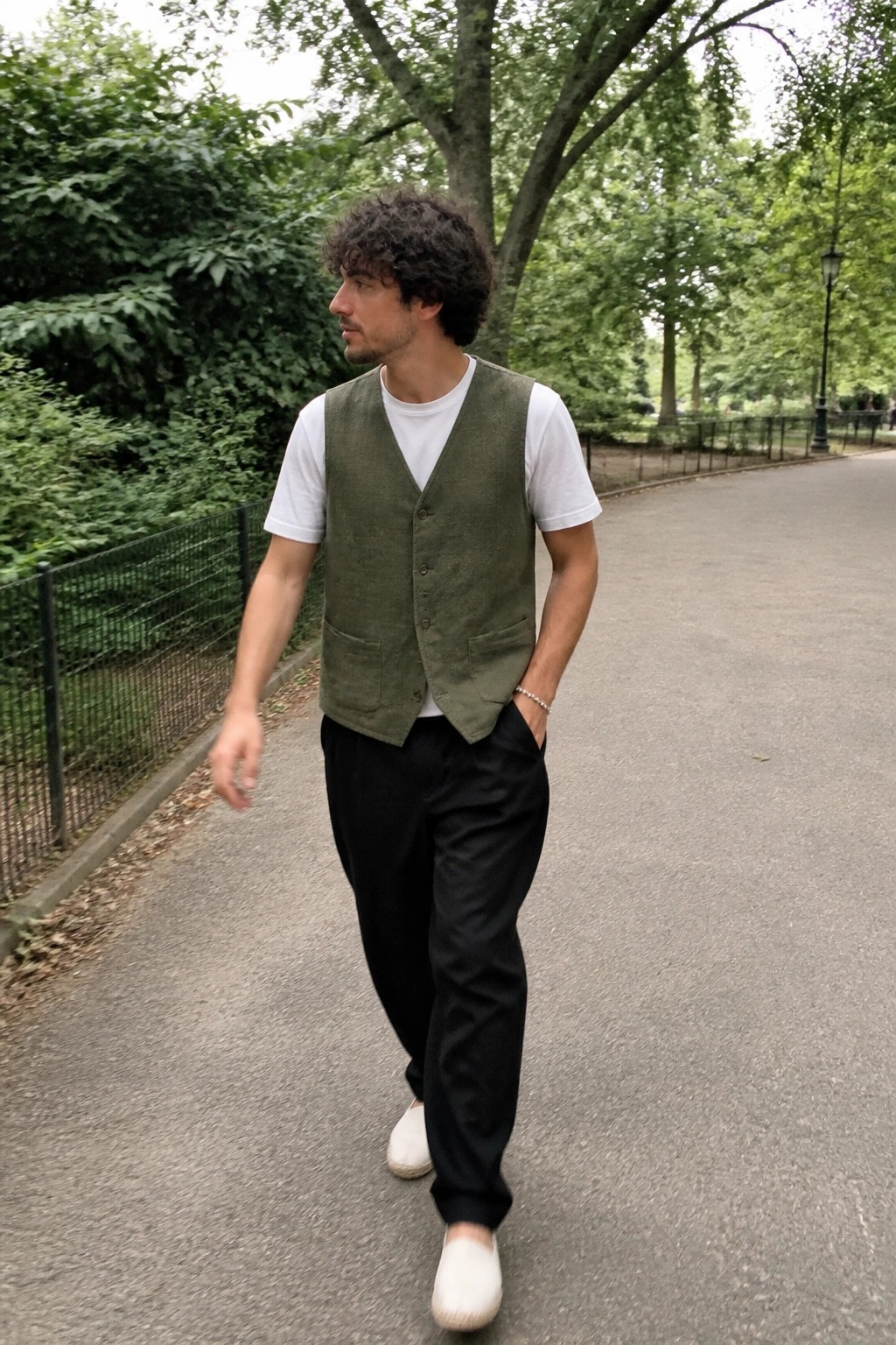 Man in green vest over white t-shirt walks on park path with hands in pockets