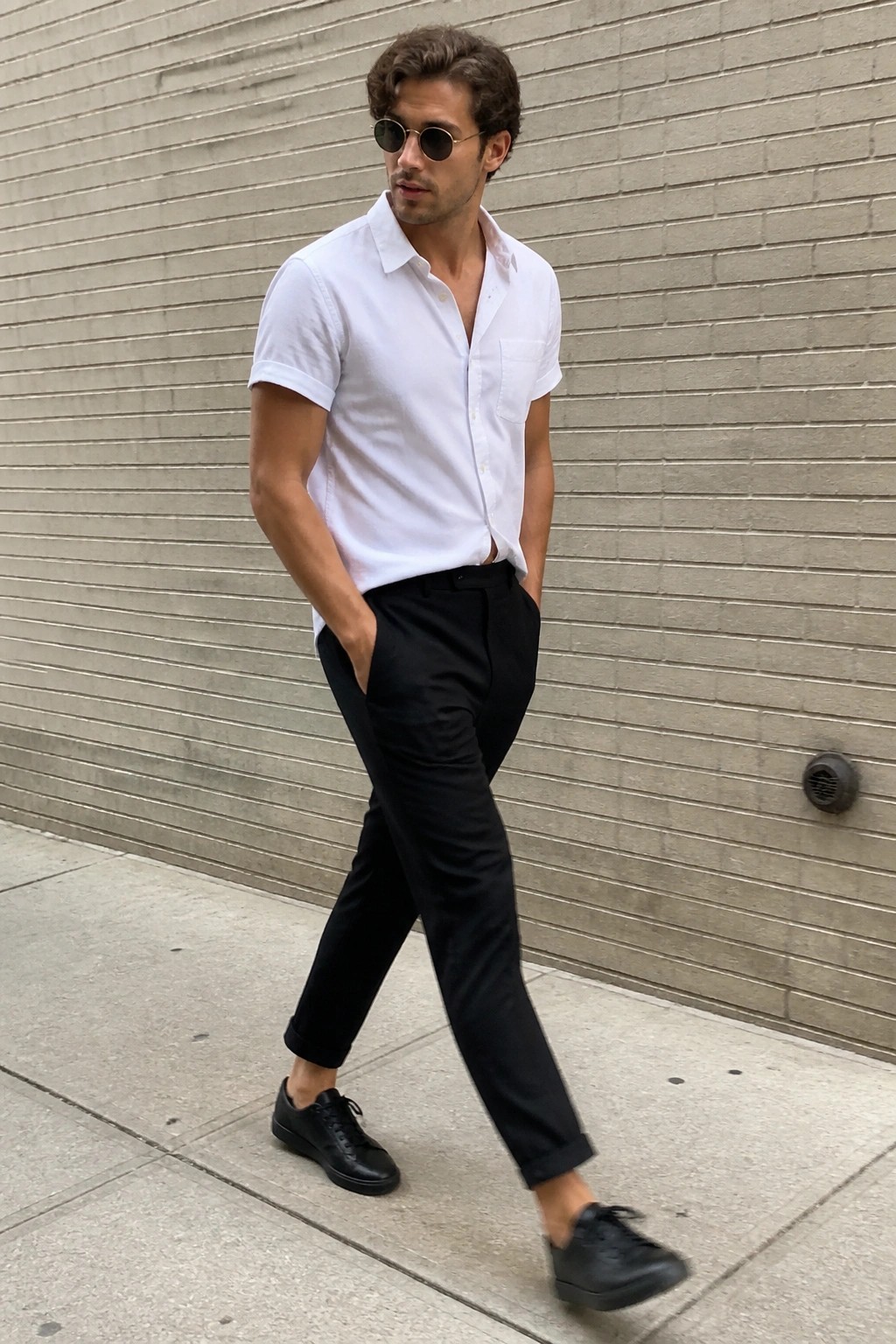 Man in white shirt and black pants walking by brick wall