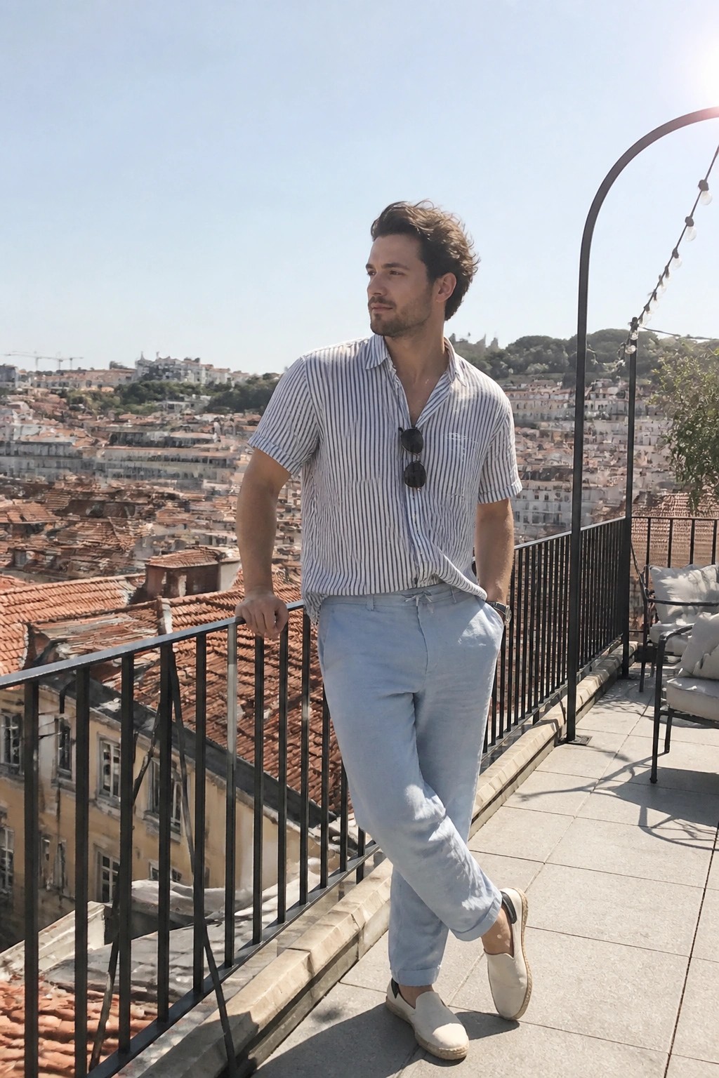 Man in striped shirt and light pants on sunny rooftop overlooking city rooftops