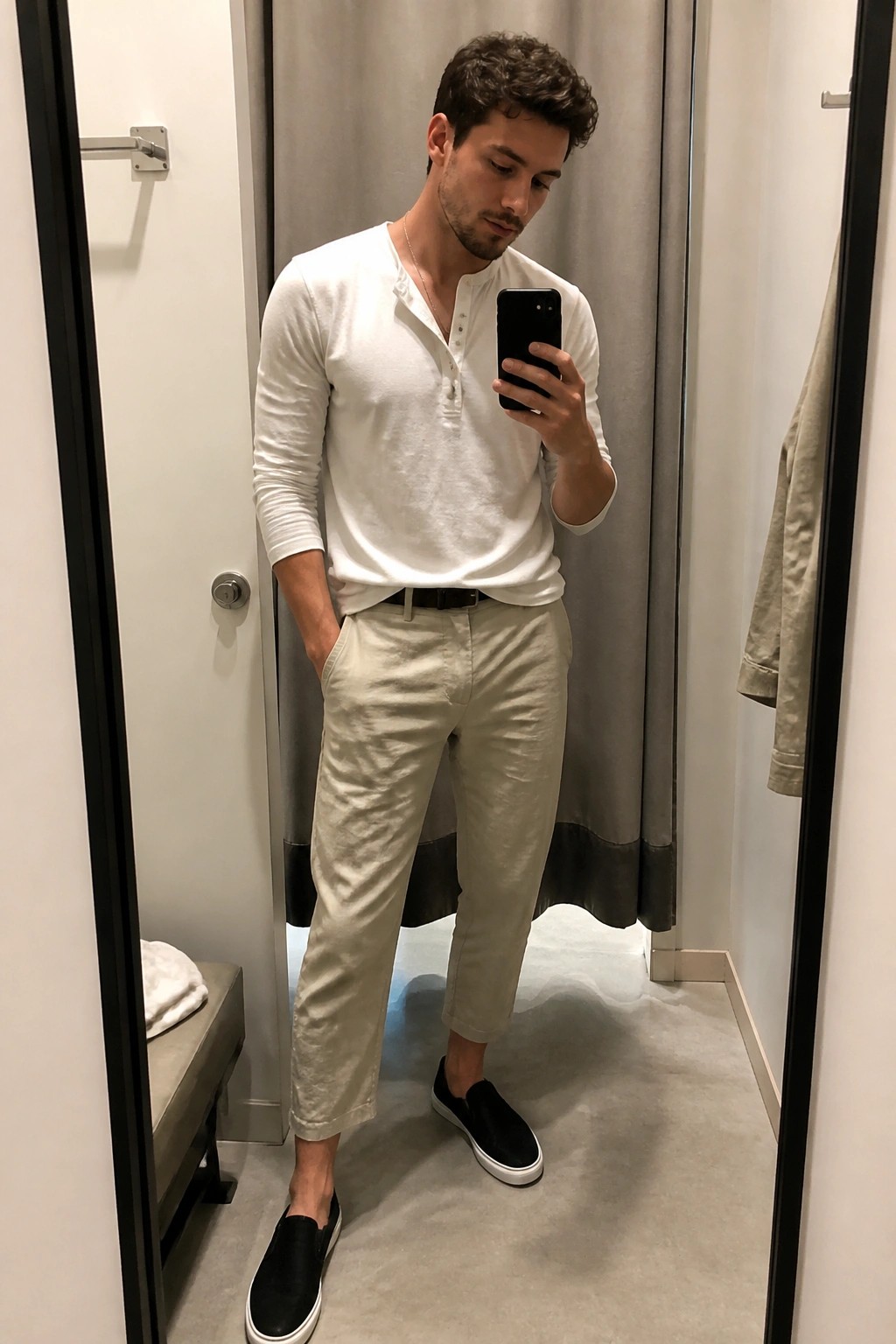 Man in mirror selfie wearing white henley shirt tucked into beige linen pants with black belt and black slip on sneakers.