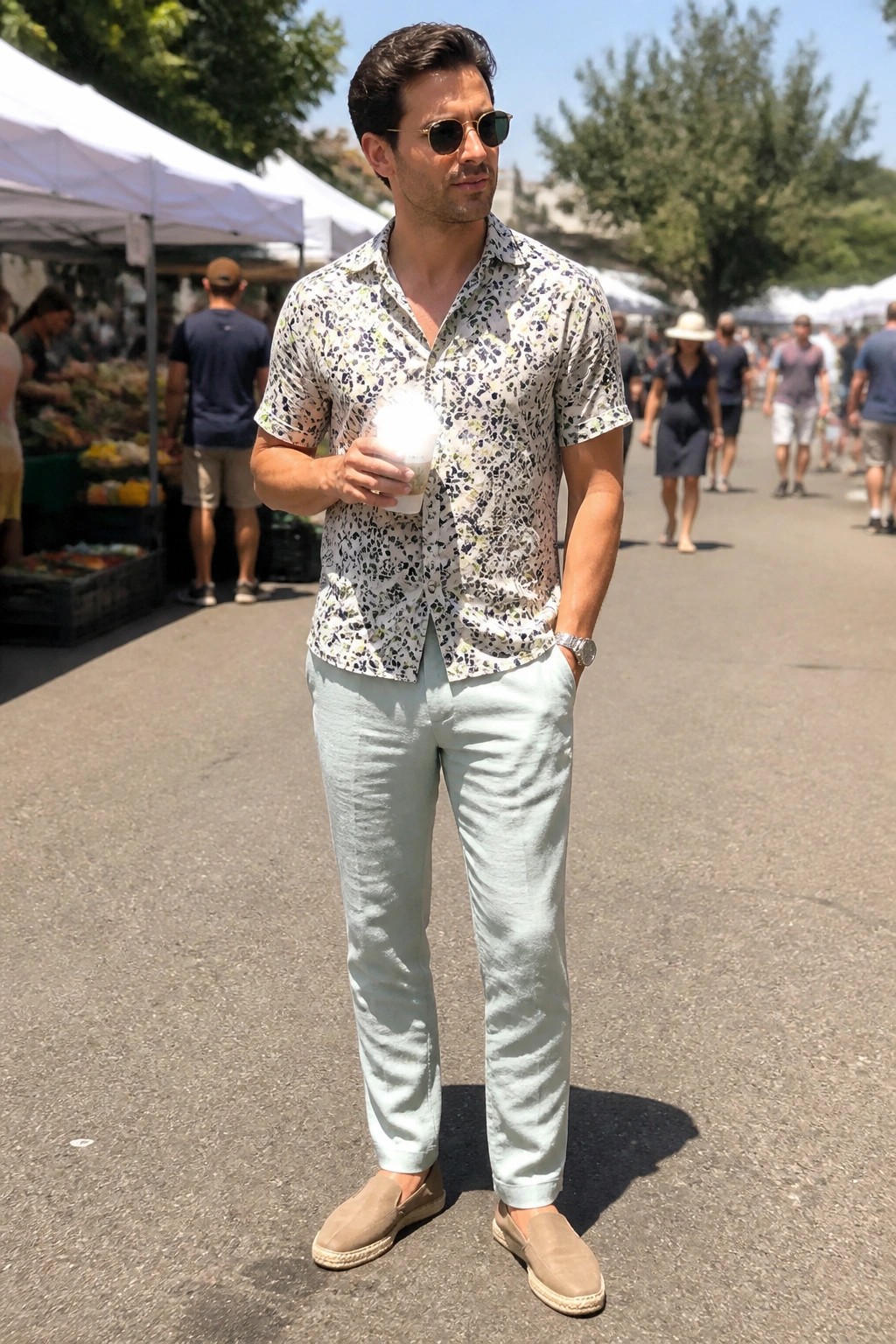 Man in patterned shirt and light green pants holding drink at sunny market