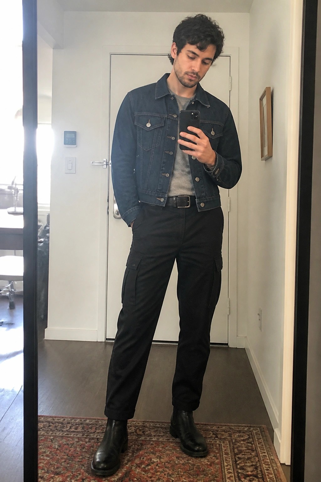Man in blue denim jacket and black cargo pants taking mirror selfie with phone