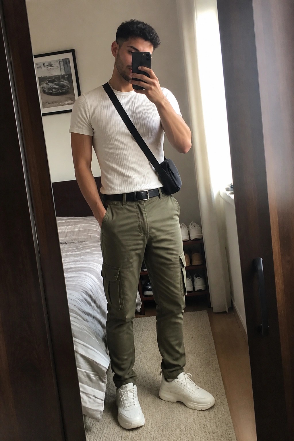 Man in white t-shirt and olive cargo pants taking a mirror selfie.