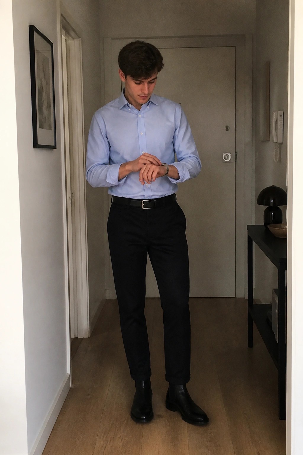 Man in light blue shirt and black pants checks watch in hallway
