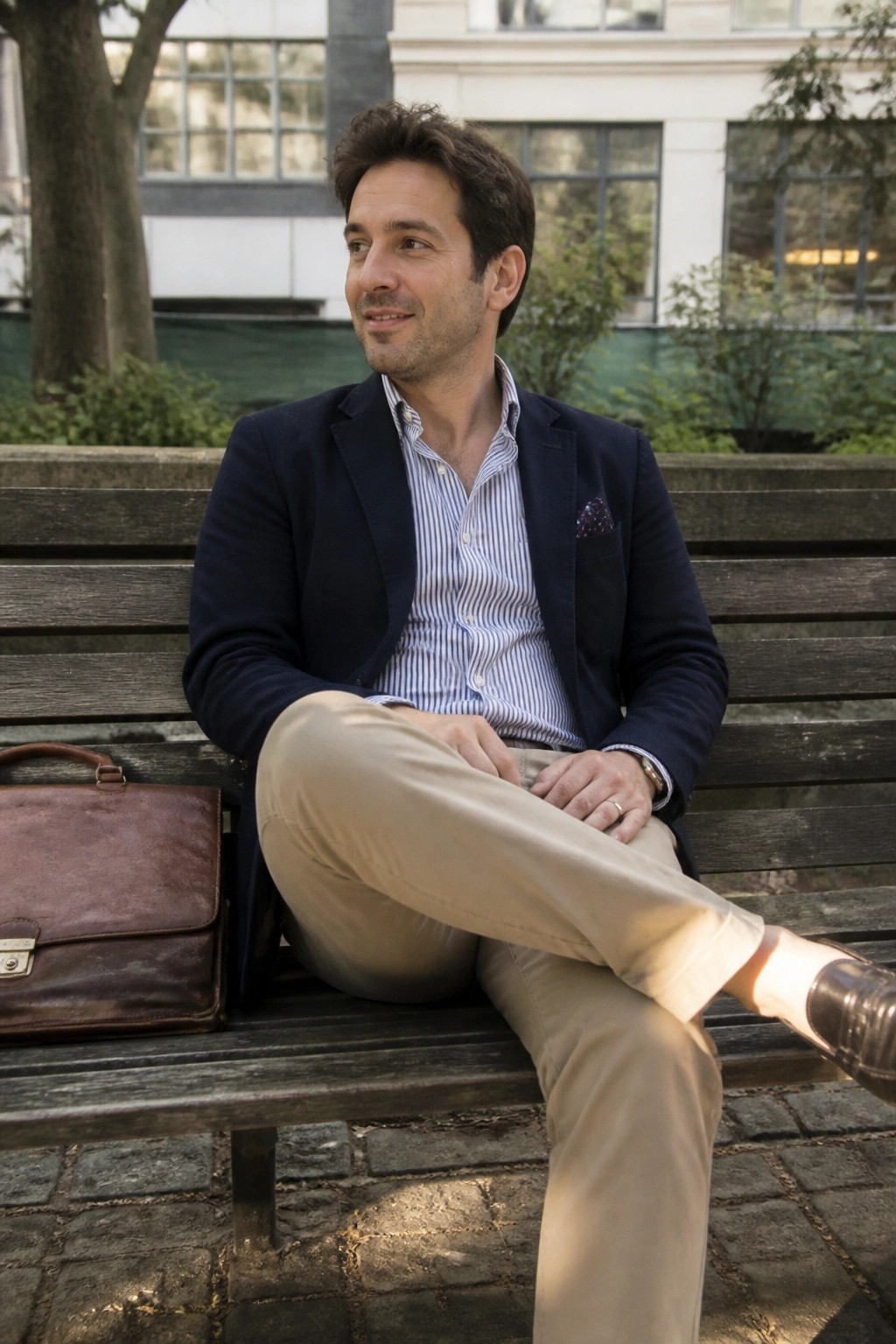 Man in navy blazer and striped shirt on wooden bench with leather briefcase