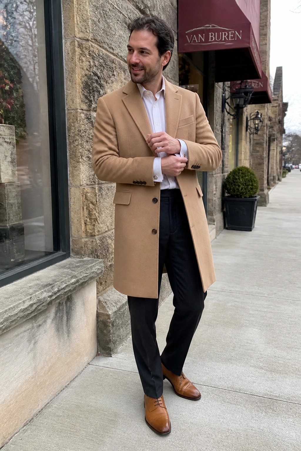 Man in tan overcoat adjusting cuffs on sidewalk by stone building