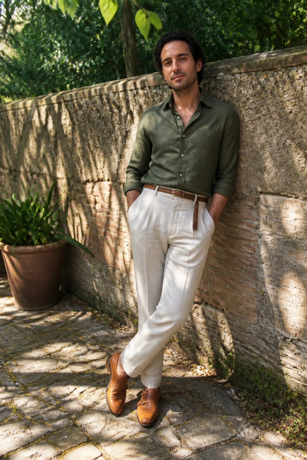 Man in green shirt and white pants leaning against stone wall outdoors