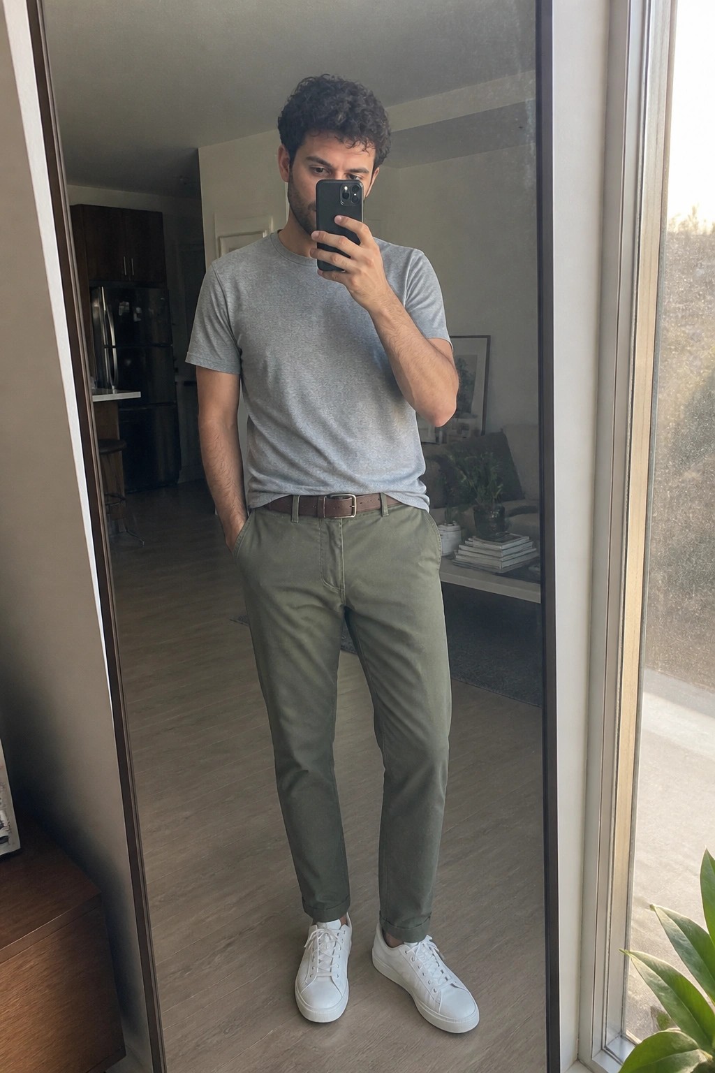Man in gray t-shirt and olive pants taking mirror selfie with phone