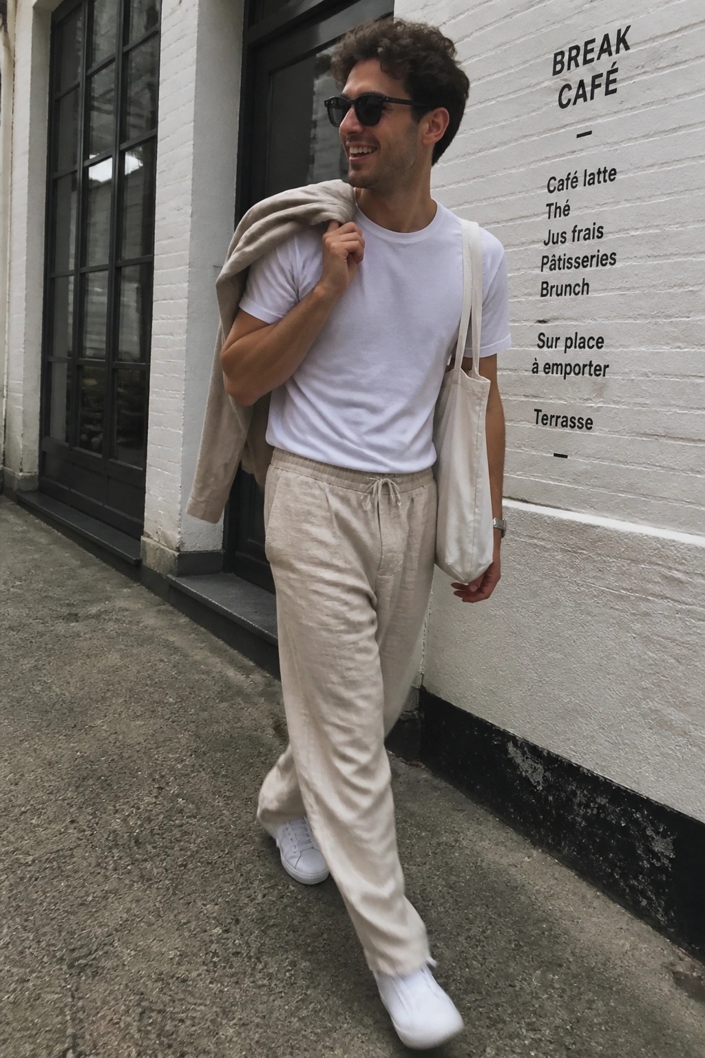 Man in white t-shirt and beige pants with tote bag outside Break Café