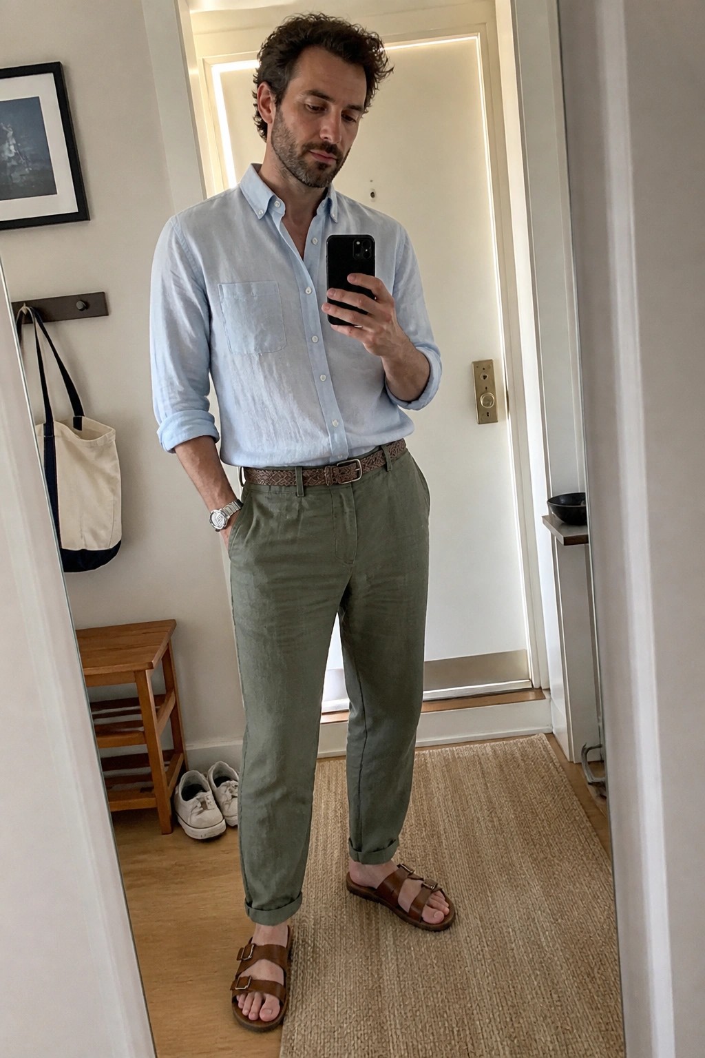 Man in light blue shirt and green pants taking mirror selfie with phone
