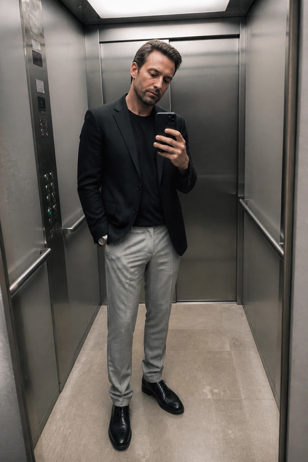 Man in black blazer and gray pants taking selfie in elevator
