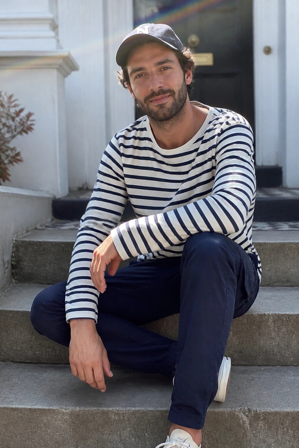 Bearded man in striped shirt and cap seated on stone steps outdoors