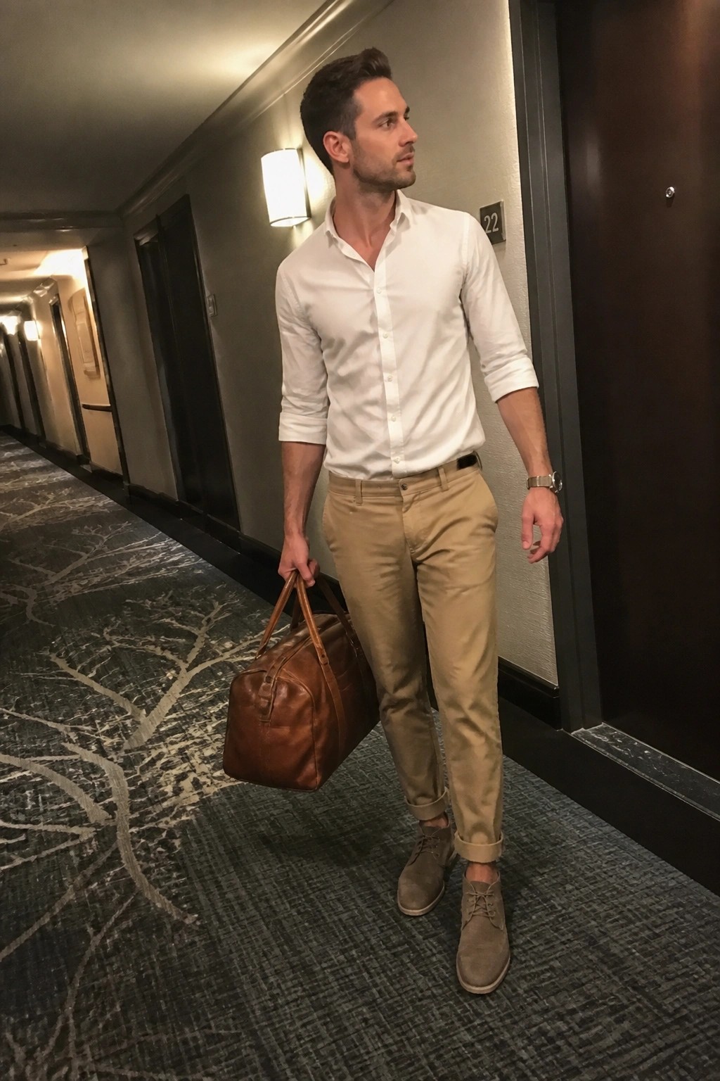 Man in white shirt and khaki pants holding brown leather bag in hallway