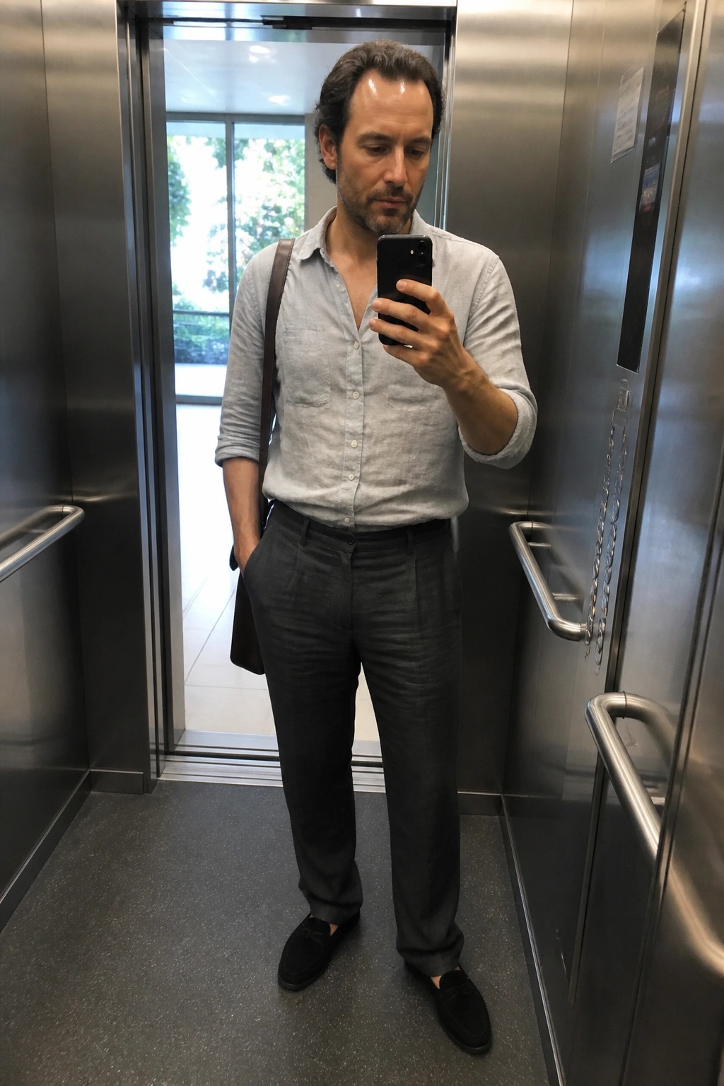 Man in light blue shirt taking selfie in open elevator with phone